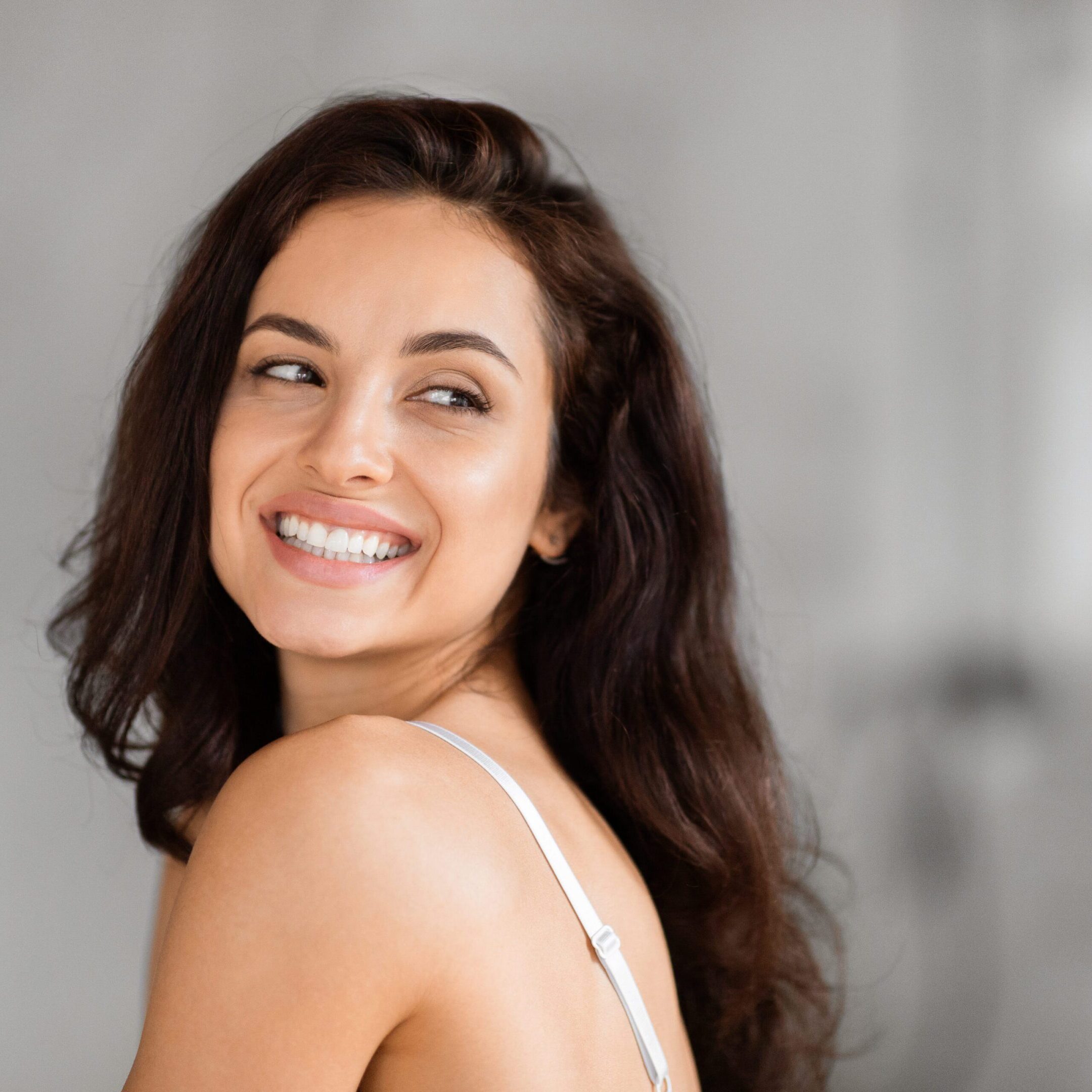 Cheerful lady glances back with a radiant smile, embodying optimism in a grayscale bathroom scene, copy space