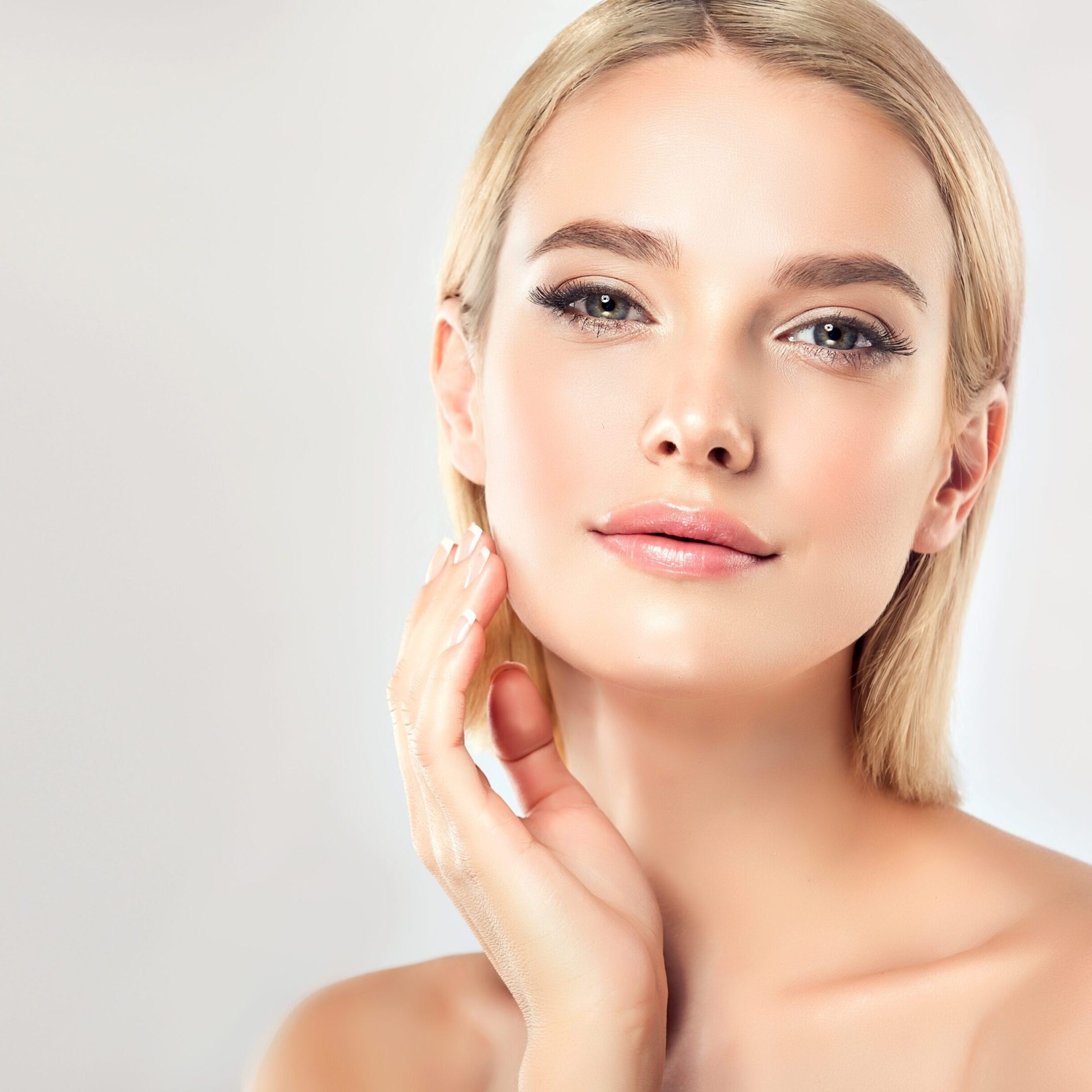 Gorgeous, young,woman with almond like eyes and fashionable hairstyle on the short blonde hair is touching tenderly the face. Facial treatment, cosmetology, beauty technologies and spa.