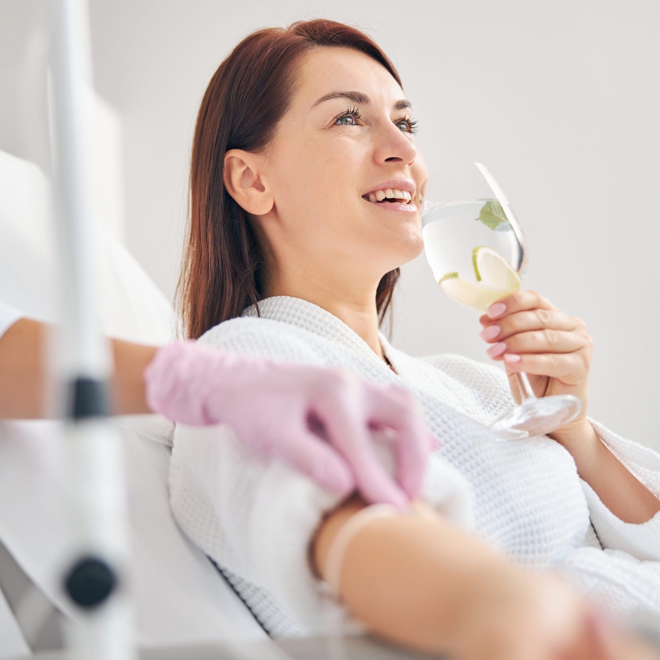 Joyous female patient drinking a healthy beverage during a medical procedure in a beauty clinic
