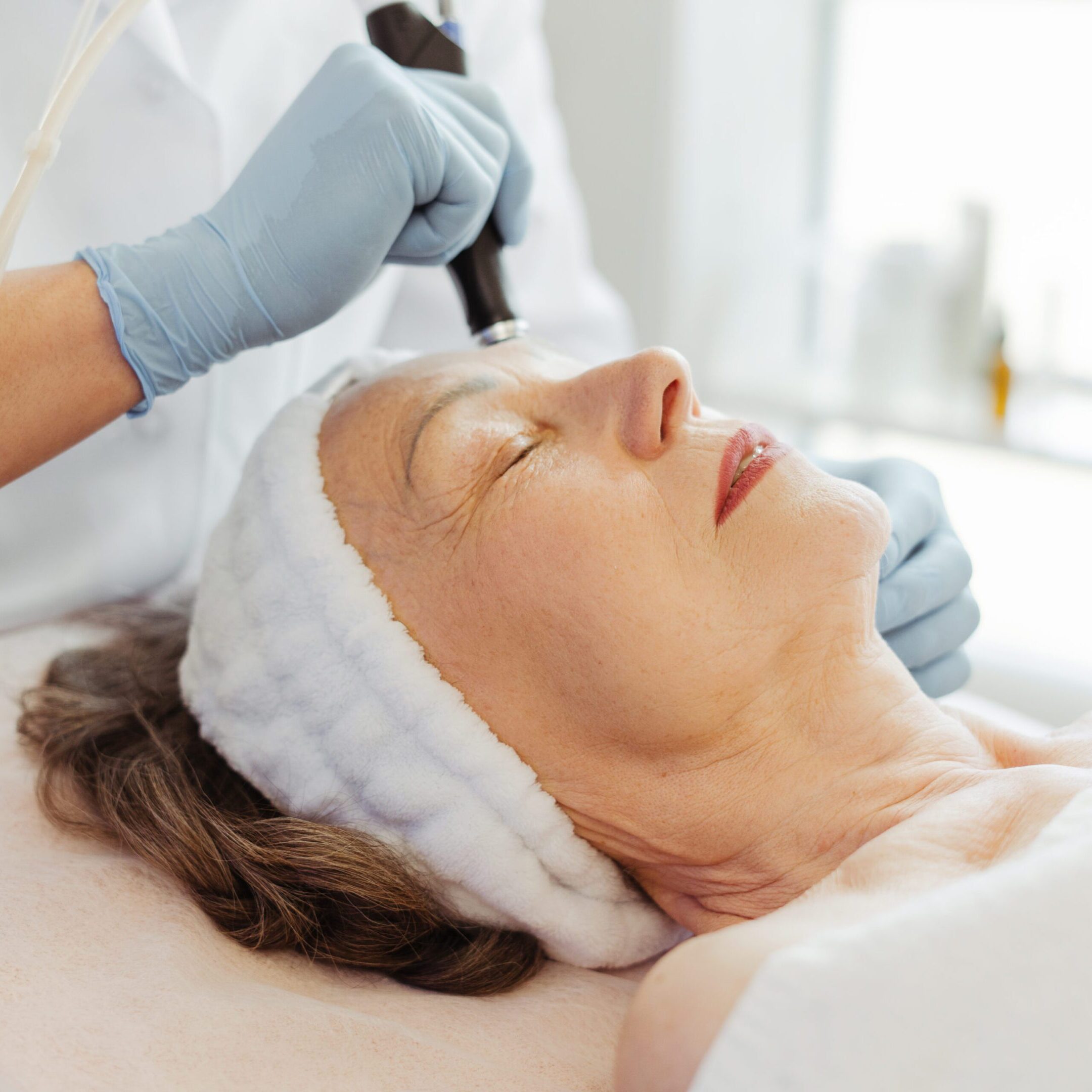 Beautician in gloves conducts vacuum cleaning and polishing face skin of senior, mature woman Closeup professional beautician in gloves conducts vacuum cleaning and polishing face skin of senior, mature woman in cosmetology clinic. Moisturizing and rejuvenating procedures. Cosmetology concept